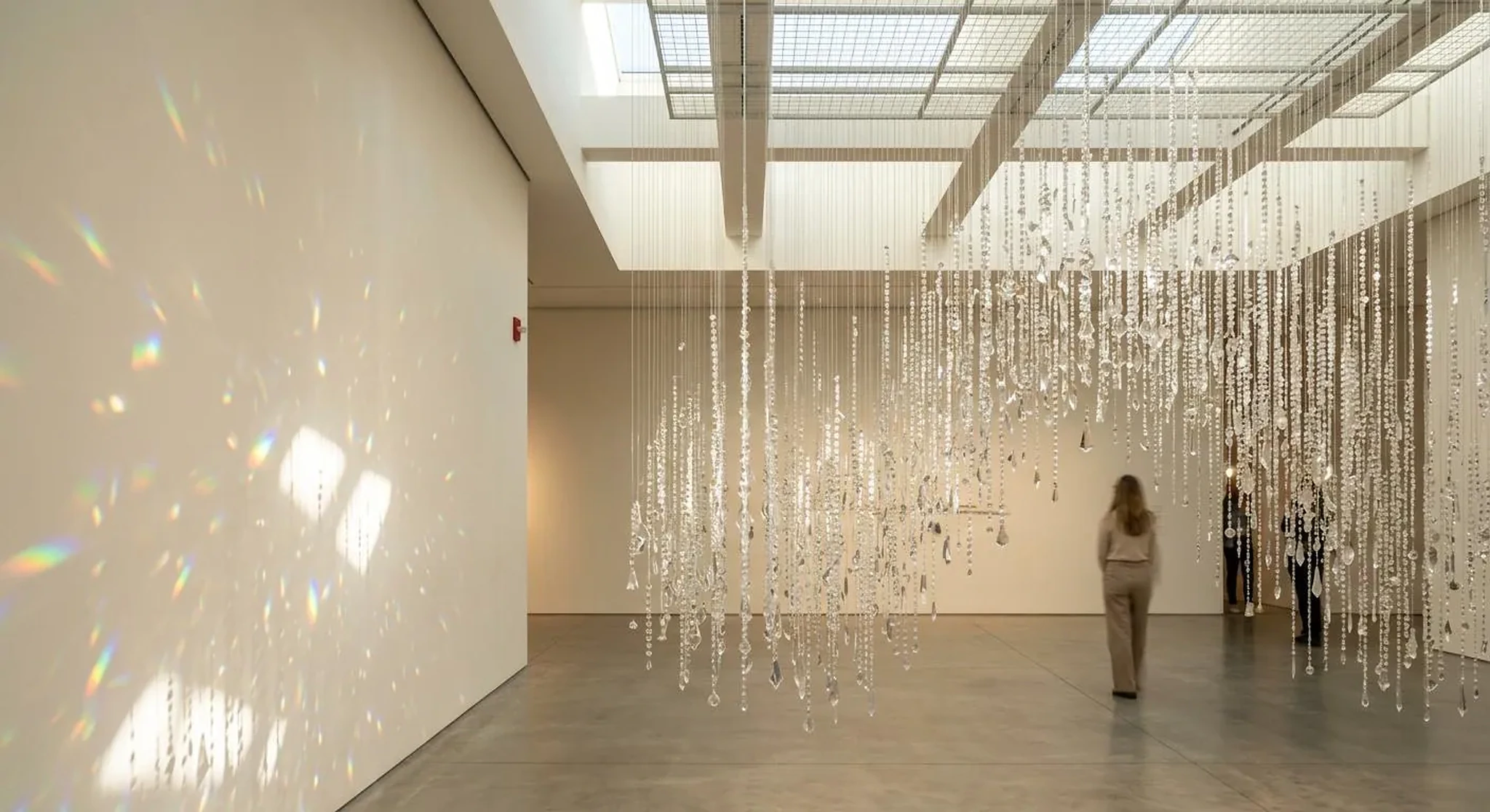 Luminous hanging crystal installation in a white gallery.
